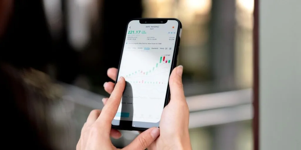 Hand hält ein Smartphone mit Marktcharts auf dem Bildschirm